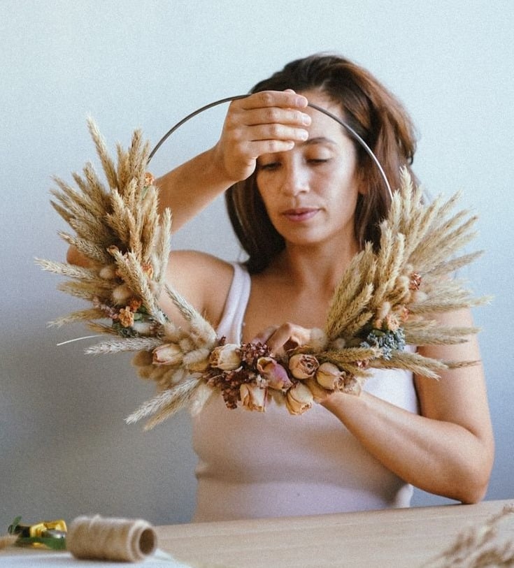 Daniela holding a handmade dried wreath of wheat, pampas and seed heads