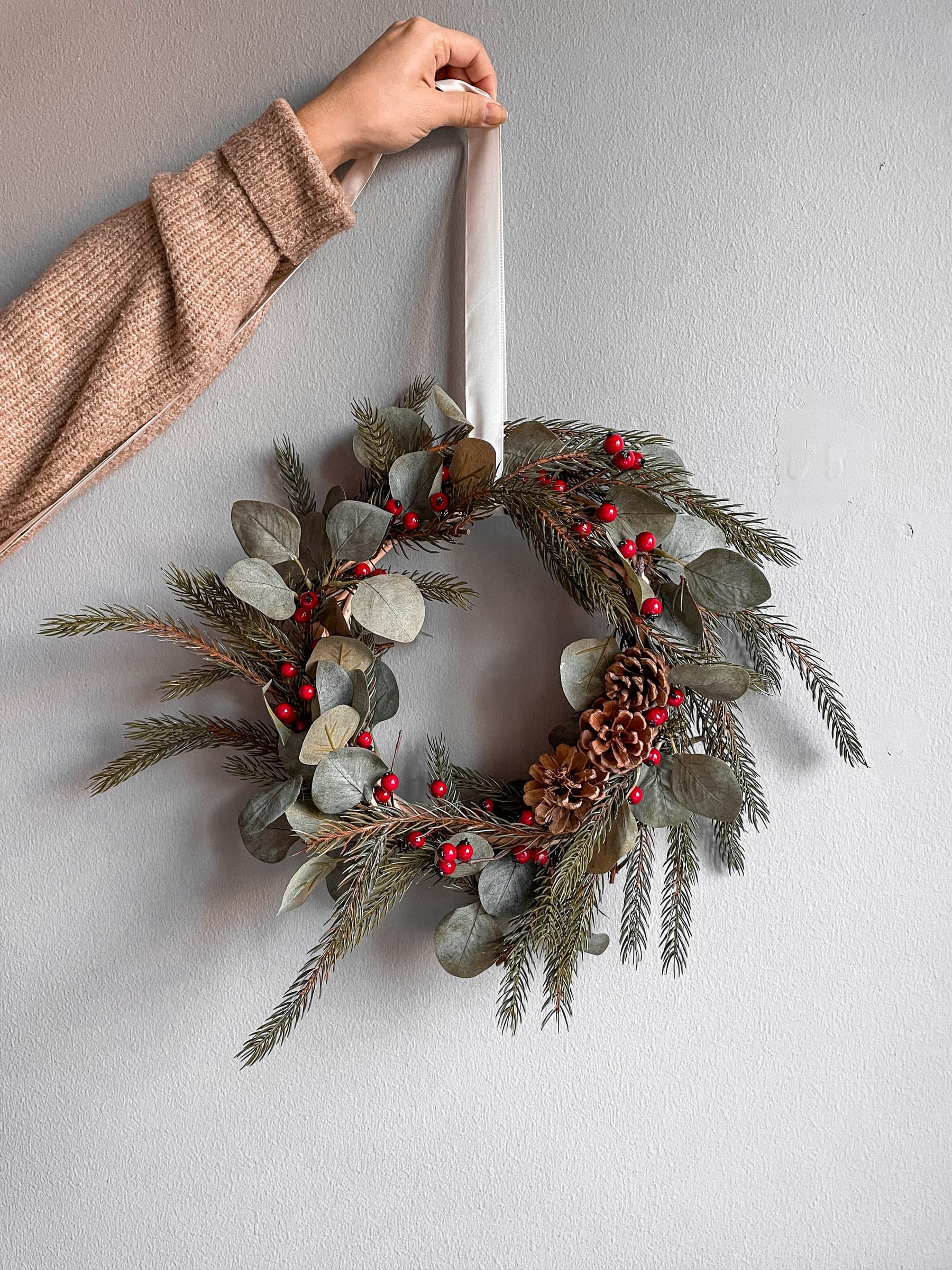 Small winter wreath of eucalyptus and red berries held against a wall